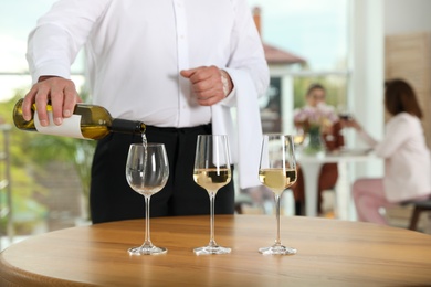 Waiter pouring wine into glass in restaurant, closeup