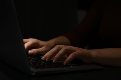 Hacker working with laptop in darkness, closeup of hands. Cyber crime