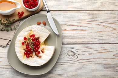 Brie cheese served with almonds, red currants and honey on white wooden table, flat lay. Space for text