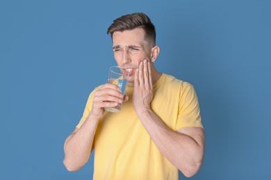 Young man with sensitive teeth and glass of cold water on color background
