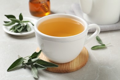 Cup of aromatic sage tea and fresh leaves on light grey table