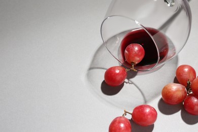 Photo of Overturned glass of wine and grapes on white background, closeup. Space for text