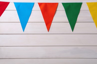 Bunting with colorful triangular flags on white wooden background. Space for text