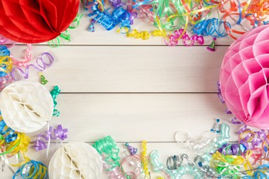 Frame of colorful serpentine streamers and other party accessories on white wooden table, flat lay. Space for text