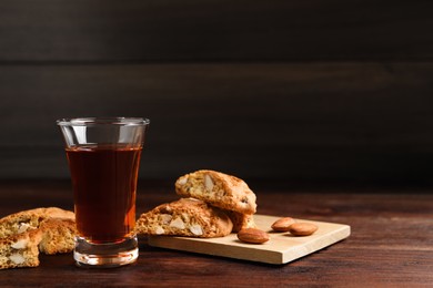 Tasty cantucci and glass of liqueur on wooden table, space for text. Traditional Italian almond biscuits