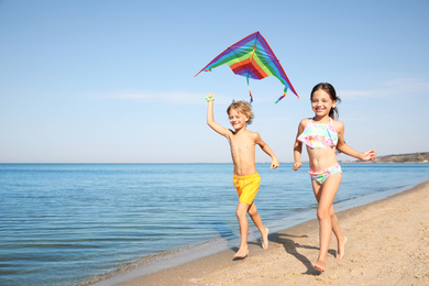 Cute little children with kite running at sandy beach on sunny day
