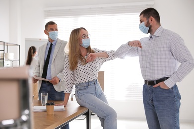 Coworkers with protective masks making elbow bump in office. Informal greeting during COVID-19 pandemic