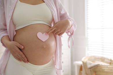 Pregnant woman with heart shaped sticky note on belly indoors, closeup. Choosing baby name