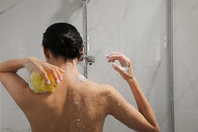 Young woman with mesh pouf taking shower at home, back view
