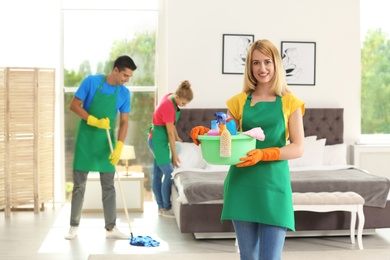 Team of professional janitors in uniform cleaning bedroom
