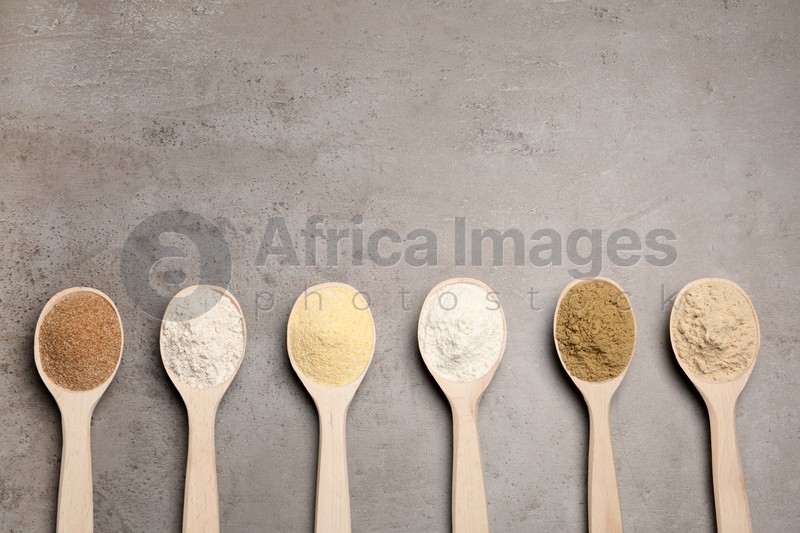 Spoons with different types of flour on table, top view. Space for text