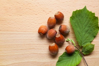 Tasty hazelnuts and green leaves on wooden table, top view. Space for text