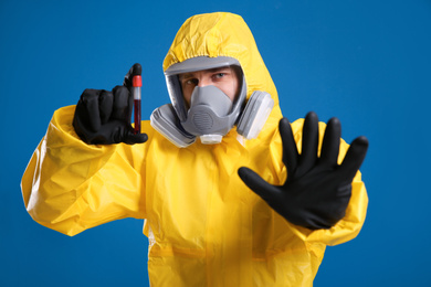 Man in chemical protective suit holding test tube of blood sample on blue background. Virus research