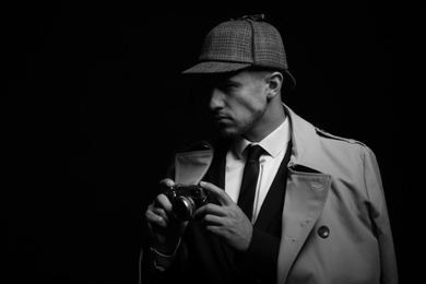 Photo of Old fashioned detective with camera on dark background, black and white effect. Space for text