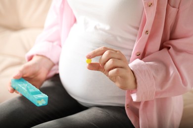 Pregnant woman holding pill on blurred background closeup