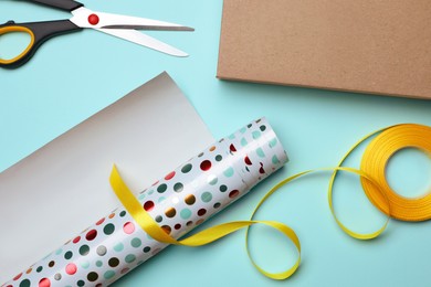 Wrapping paper roll, ribbon, scissors and box on turquoise background, flat lay