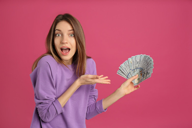 Surprised young woman with cash money on pink background