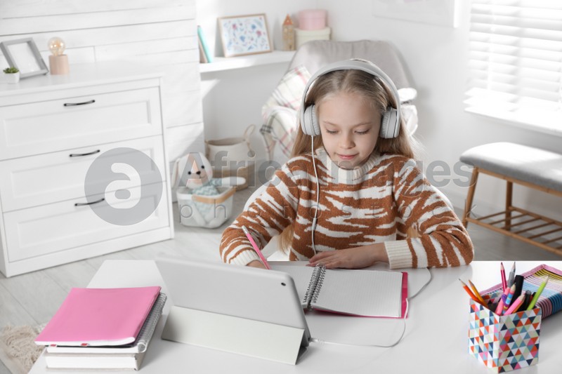 Photo of Cute little girl with modern tablet studying online at home. E-learning
