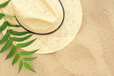 Straw hat and green leaves on sandy beach, flat lay. Space for text