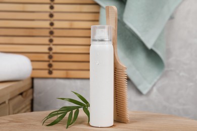 Dry shampoo spray, green leaves and comb on wooden table in bathroom