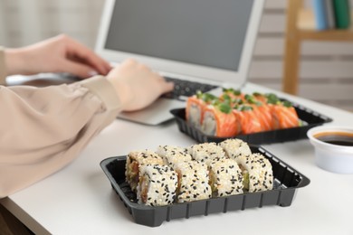 Woman using laptop in office, focus on tasty sushi rolls. Lunch break at work