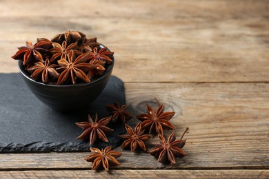Aromatic anise stars with bowl on wooden table. Space for text