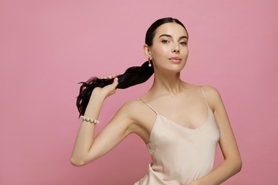 Young woman wearing elegant pearl jewelry on pink background