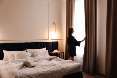 Beautiful young woman wearing silk robe near window in hotel room