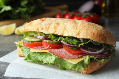 Delicious sandwich with fresh vegetables and salami on table