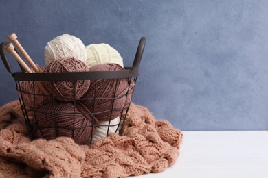 Photo of Woolen yarns with knitting needles in basket and sweater on white wooden table. Space for text
