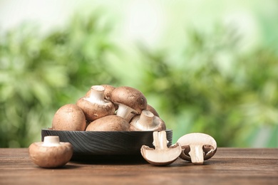 Plate of fresh champignon mushrooms on wooden table against blurred background