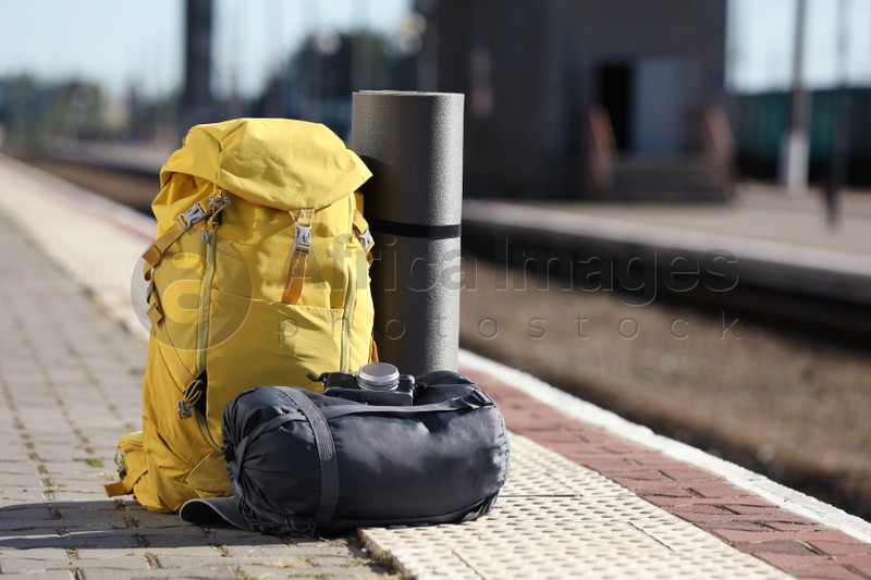 Stylish backpack, sleeping bag, camera and camping mat on railway platform outdoors. Tourism concept