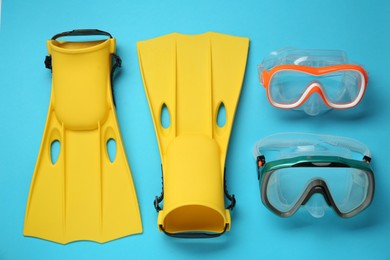 Pair of yellow flippers and masks on light blue background, flat lay