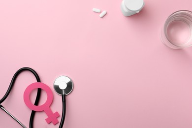 Female gender sign, stethoscope, pills and glass of water on pink background, flat lay. Space for text