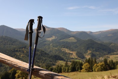 Photo of Trekking poles near wooden railing and picturesque view of mountain landscape as background. Space for text
