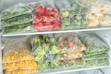 Plastic bags with different frozen vegetables in refrigerator
