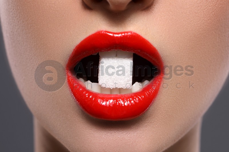 Closeup view of young with beautiful lips eating sugar cube on grey background