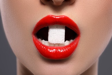 Closeup view of young with beautiful lips eating sugar cube on grey background