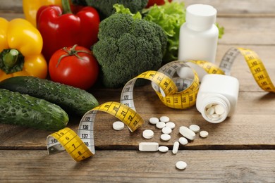 Weight loss pills, different vegetables and measuring tape on wooden table