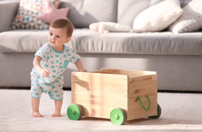 Cute baby holding on to wooden cart in living room. Learning to walk