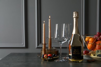 Bottle of sparkling wine, glasses, candles and delicious snacks on grey table. Space for text