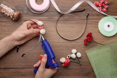Woman with hot glue gun making craft at wooden table, top view