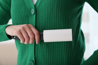 Photo of Woman cleaning green jacket with lint roller on light background, closeup