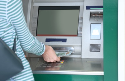 Woman taking money from cash machine outdoors, closeup. Space for text