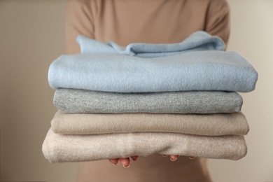 Photo of Woman with folded cashmere clothes on beige background, closeup