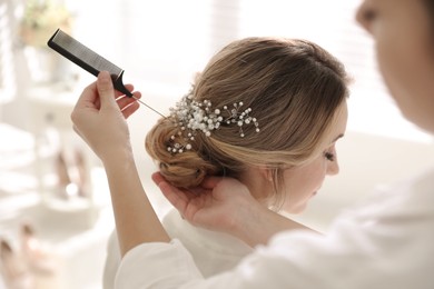 Professional stylist making wedding hairstyle for bride in salon
