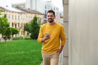 Photo of Handsome man with smartphone walking on city street