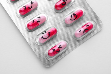 Photo of Blister of antidepressant pills with emotional faces on white background, top view