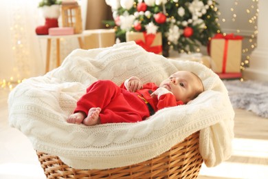 Cute little baby on knitted blanket in room decorated for Christmas