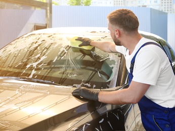 Young worker cleaning automobile with sponge at car wash
